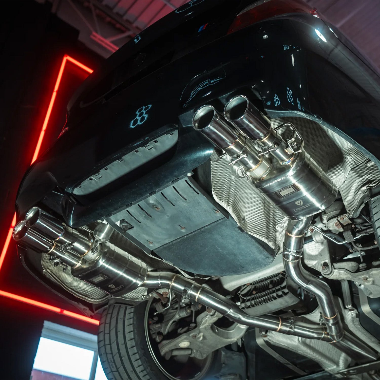 Close-up of a BMW E60 M5 Valvetronic exhaust system with a red neon light in the background